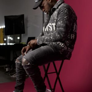 Stylish man in trendy attire sits against a red backdrop, showcasing urban fashion.