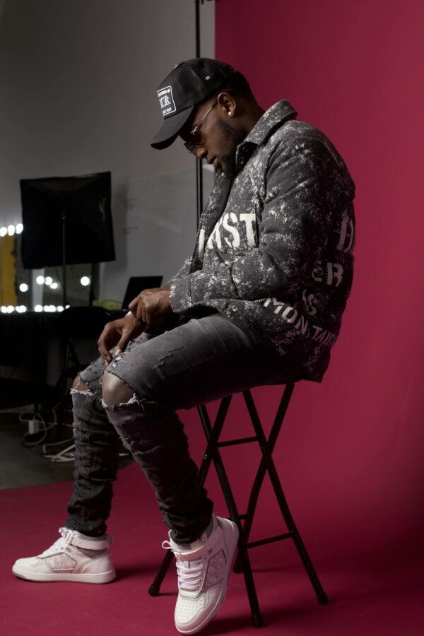 Stylish man in trendy attire sits against a red backdrop, showcasing urban fashion.