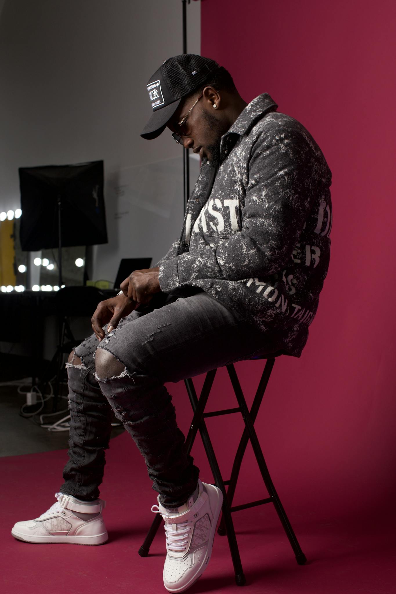 Stylish man in trendy attire sits against a red backdrop, showcasing urban fashion.