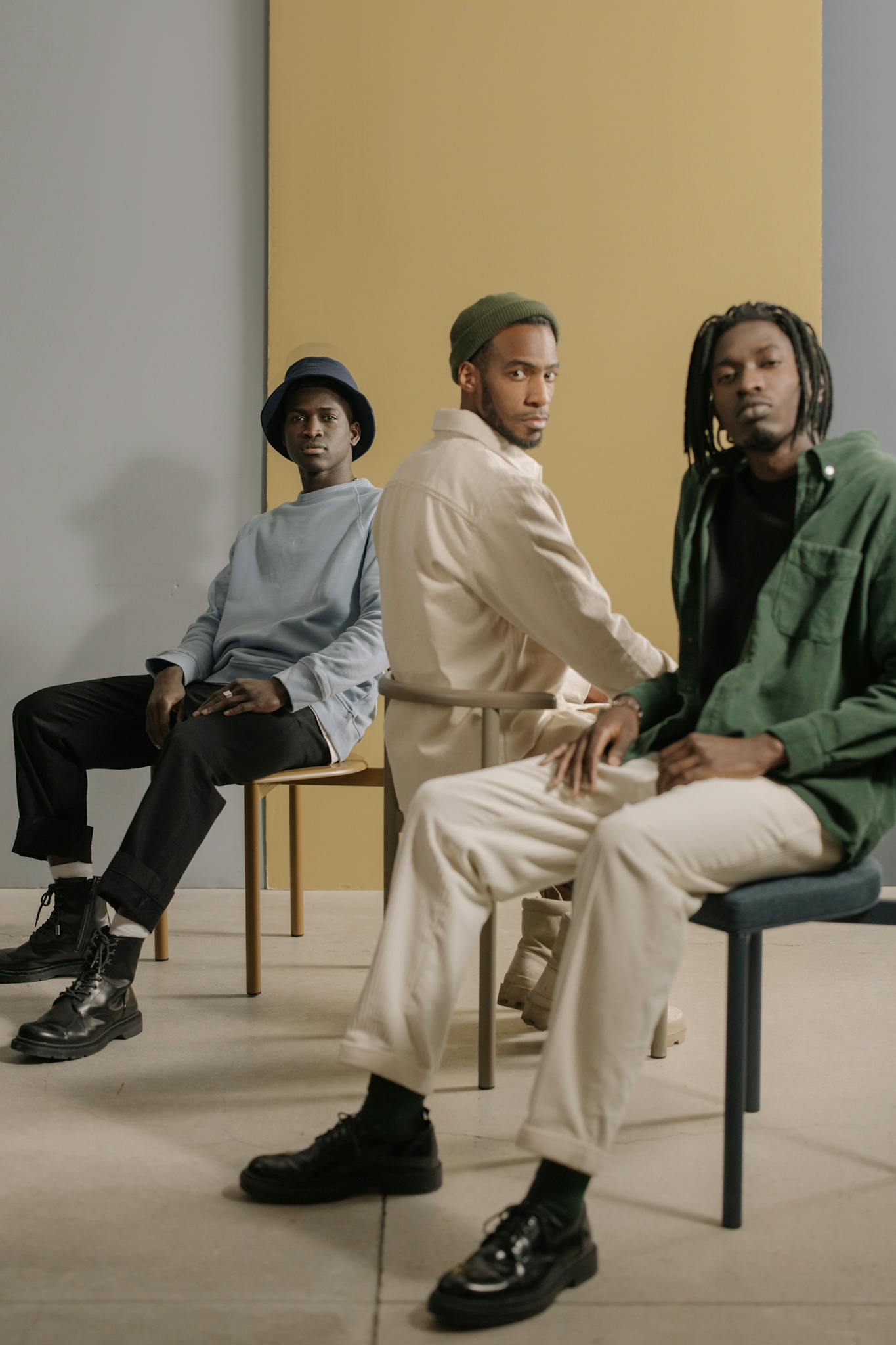 Three stylish men in modern casual wear posing indoors against a minimalist backdrop.